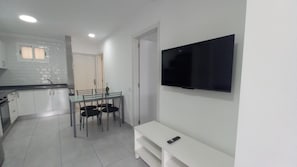 Una cucina moderna con mobili bianchi, un tavolo da pranzo con sedie, un televisore montato a parete e una panca bianca.