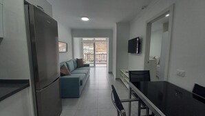 A modern kitchen with a refrigerator, a dining area with a table and chairs, a sofa, and a TV mounted on the wall. - Vacation Home 'Apartamento Sol 523 Puerto Feliz' with Sea View, Wi-Fi and Air Conditioning (Puerto Rico)