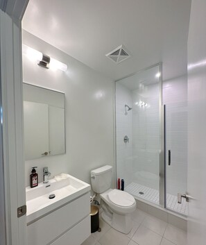 Features a sleek design with a large mirror, toilet with gold accent, and glass-enclosed shower area.