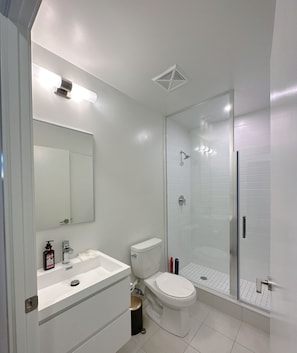 Features a sleek design with a large mirror, toilet with gold accent, and glass-enclosed shower area.