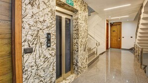 Un ascenseur moderne avec un mur en marbre, une porte en bois et une pancarte indiquant « ASCENSEUR ».