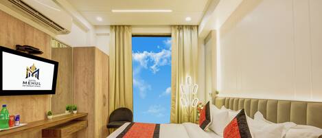 A hotel room with a bed, a TV, a desk, and a view of the sky.