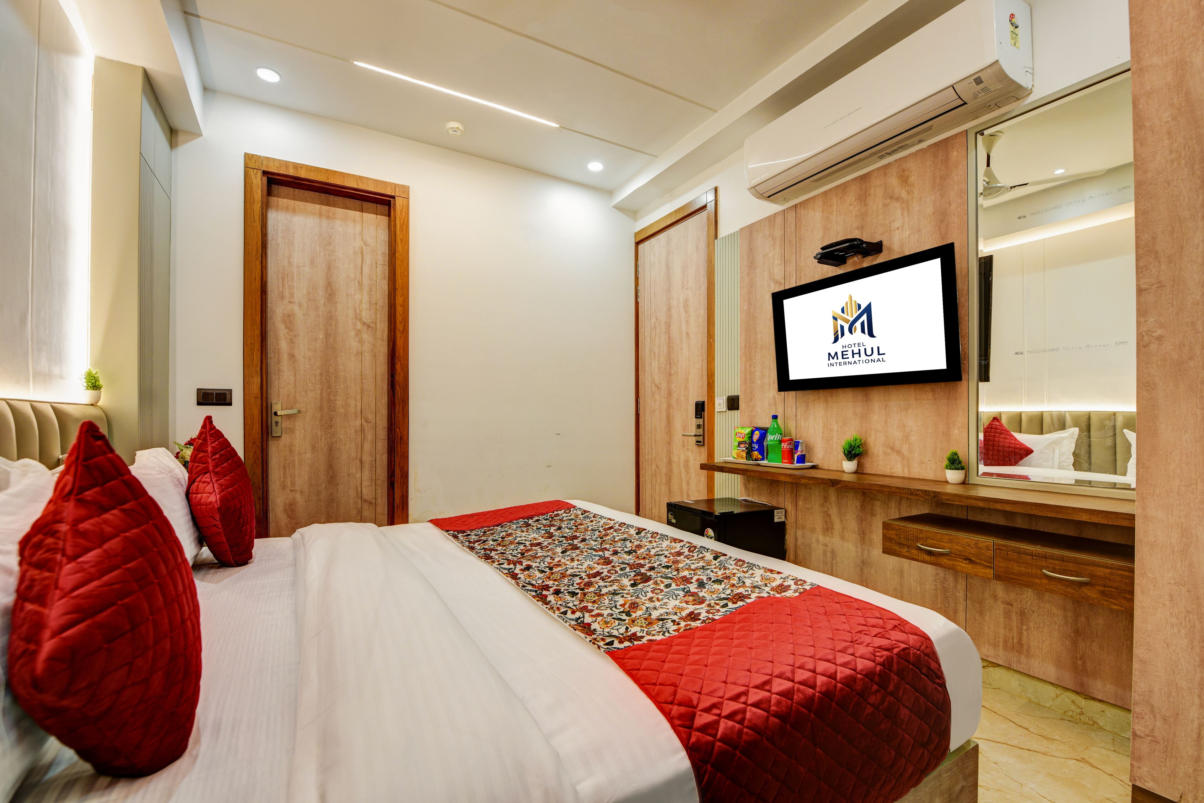 A hotel room with a bed, a TV mounted on the wall, and a wooden wardrobe.