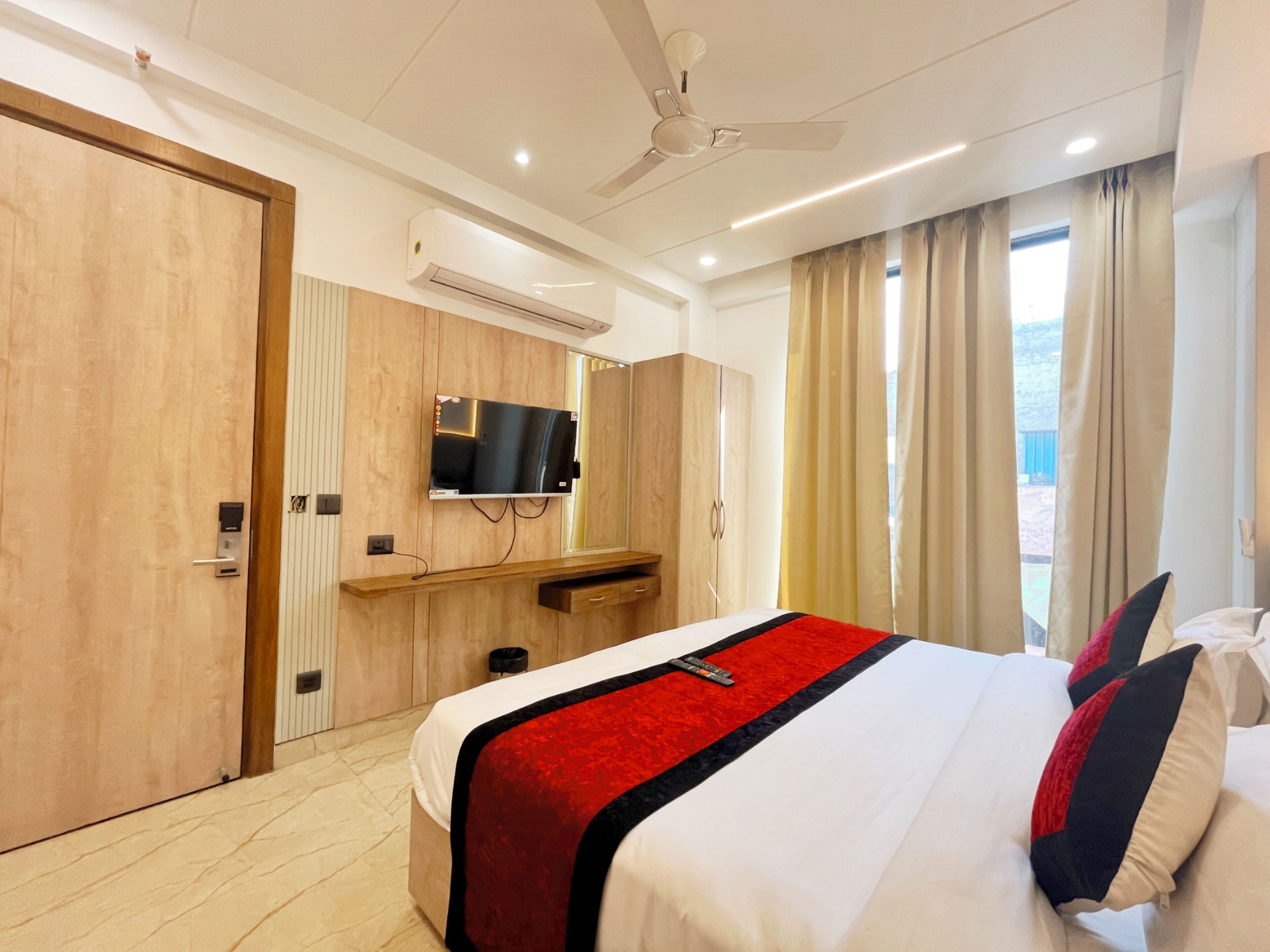 A modern hotel room with a large bed, a mounted TV, a ceiling fan, and a view of the outdoors through the window.