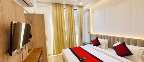 Una habitación de hotel con una cama, un televisor montado en la pared, un ventilador de techo y una ventana con cortinas.