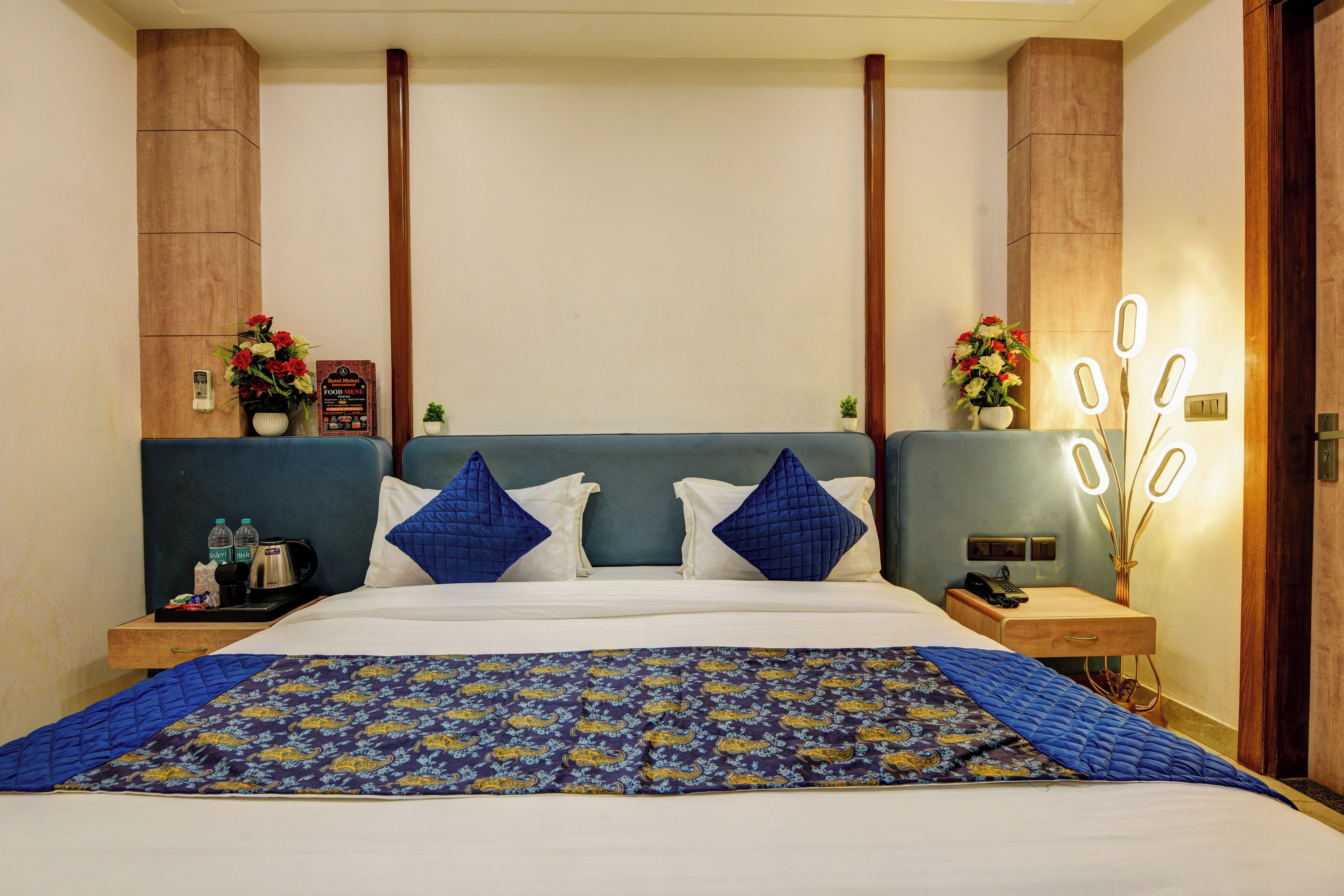 A hotel room with a large bed, two nightstands, a wooden headboard, and a wall-mounted light fixture.