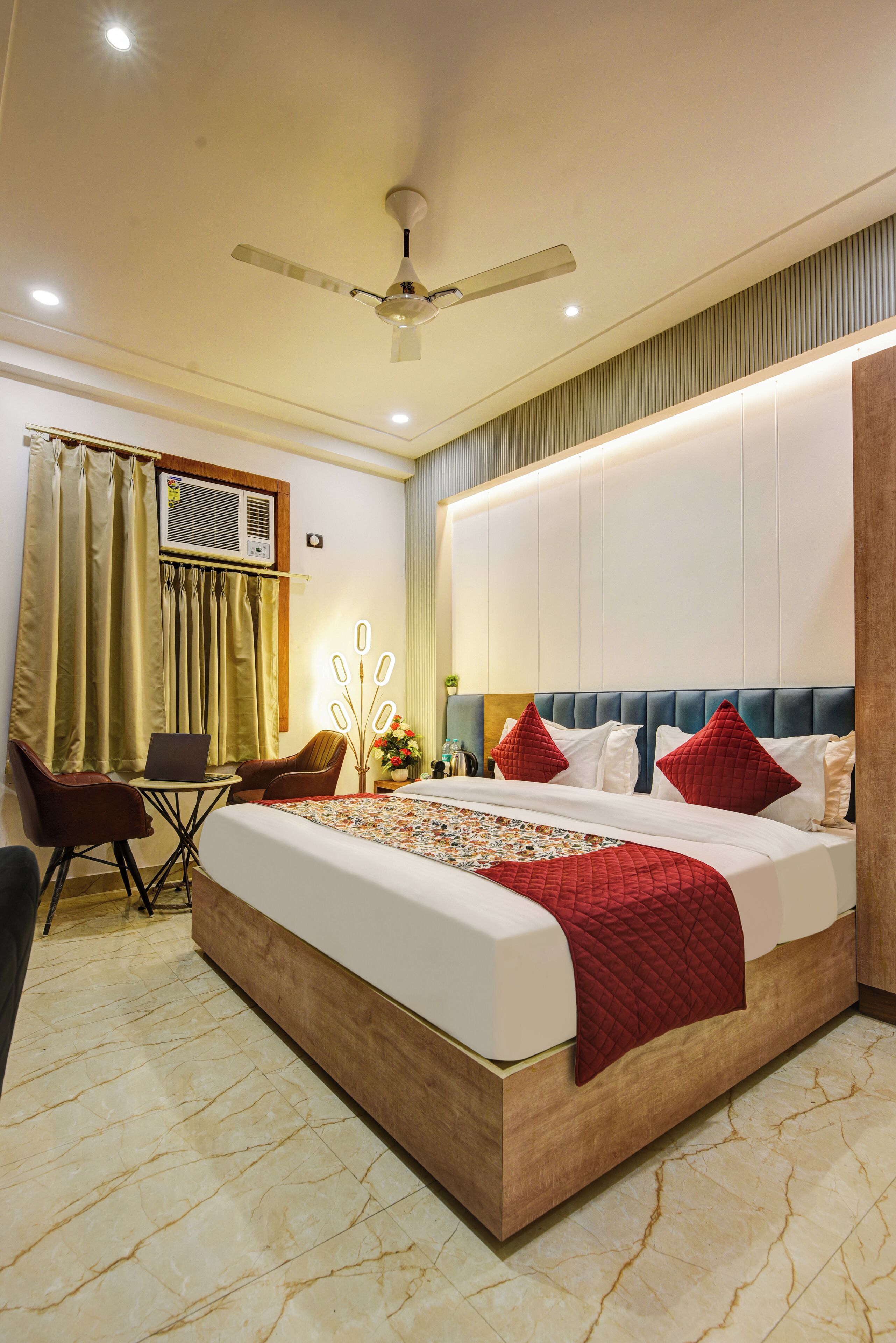 A modern hotel room with a large bed, a desk with a laptop, a ceiling fan, and a window with curtains.
