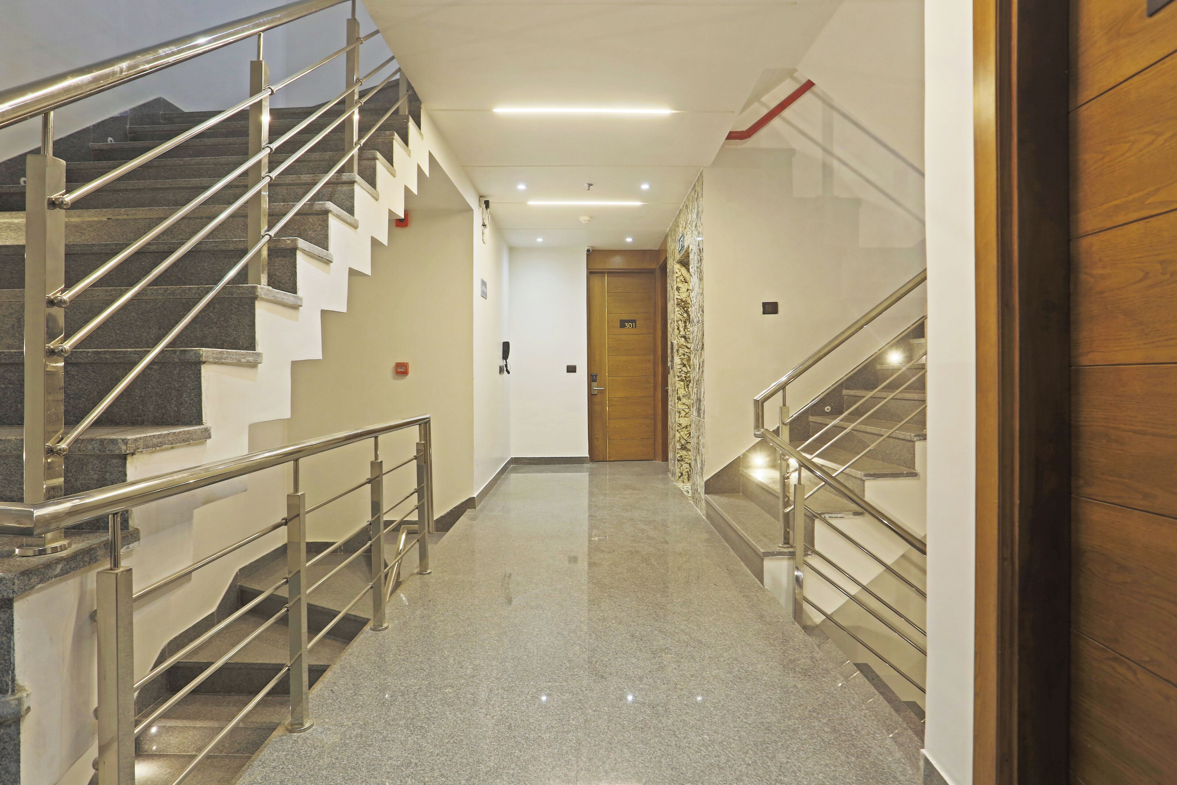A modern hotel corridor with a polished granite floor, metal handrails, and a wooden door at the end.