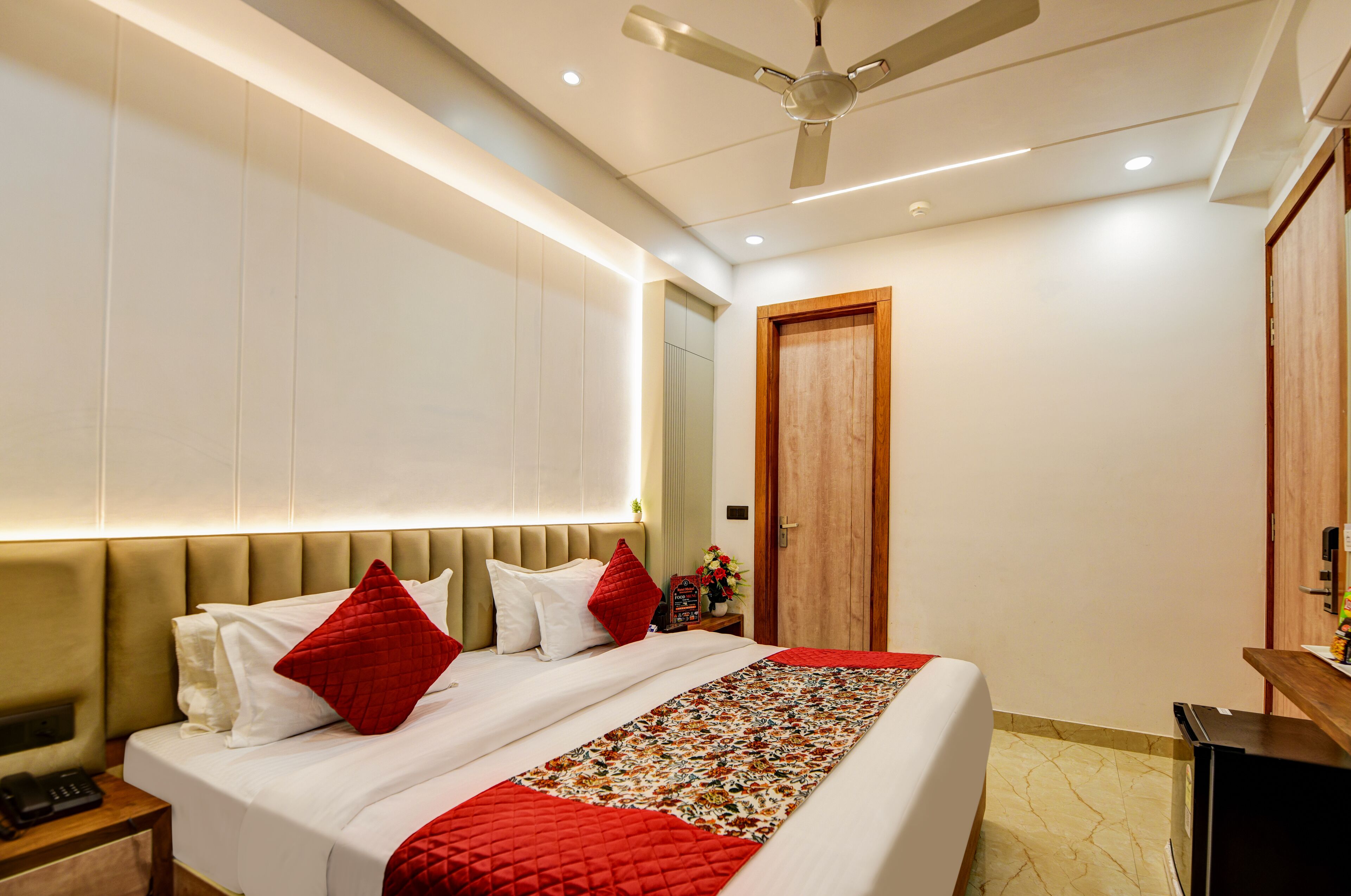 A modern hotel room with a large bed, a wooden door, and a ceiling fan.