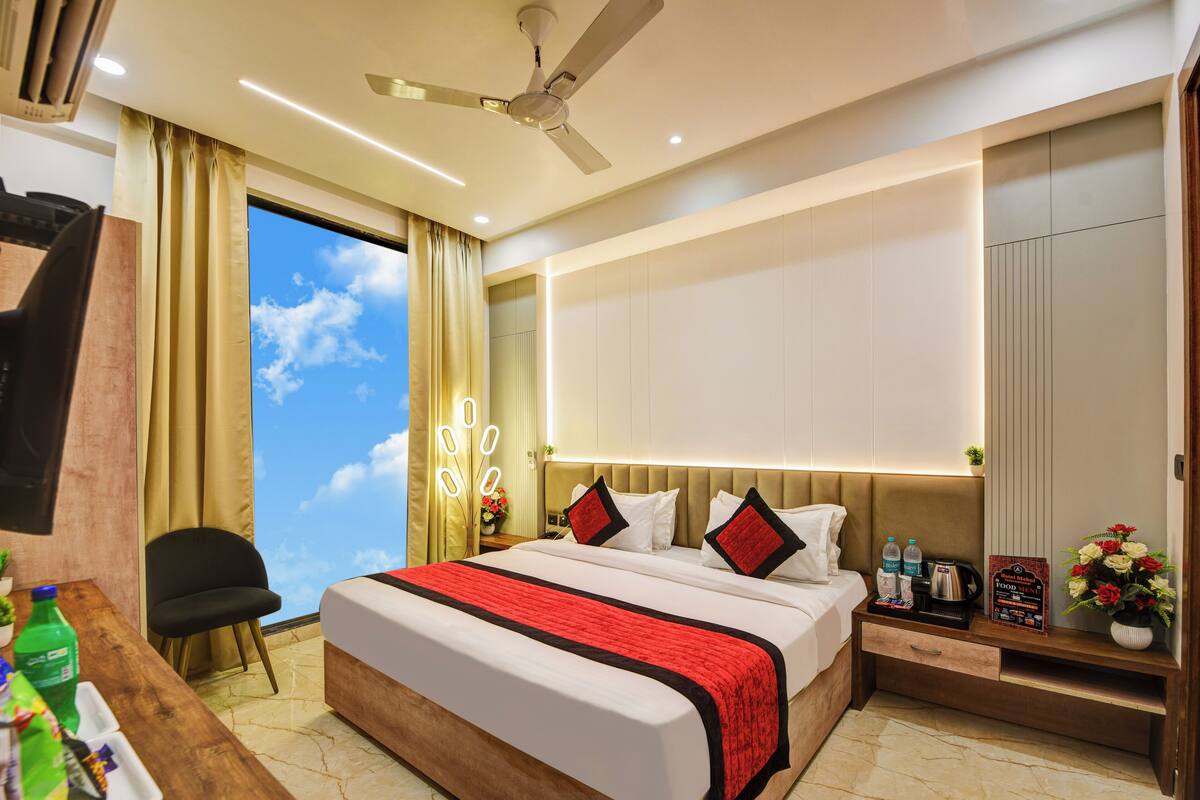 Una habitación de hotel moderna con una cama grande, un escritorio con silla, un ventilador de techo y vistas al cielo a través de una ventana.