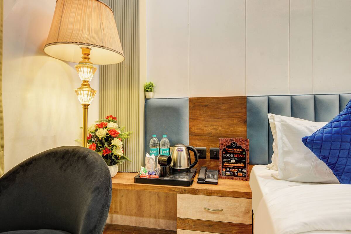 Habitación de hotel con escritorio de madera, lámpara, teléfono, cafetera y cartel de menú.