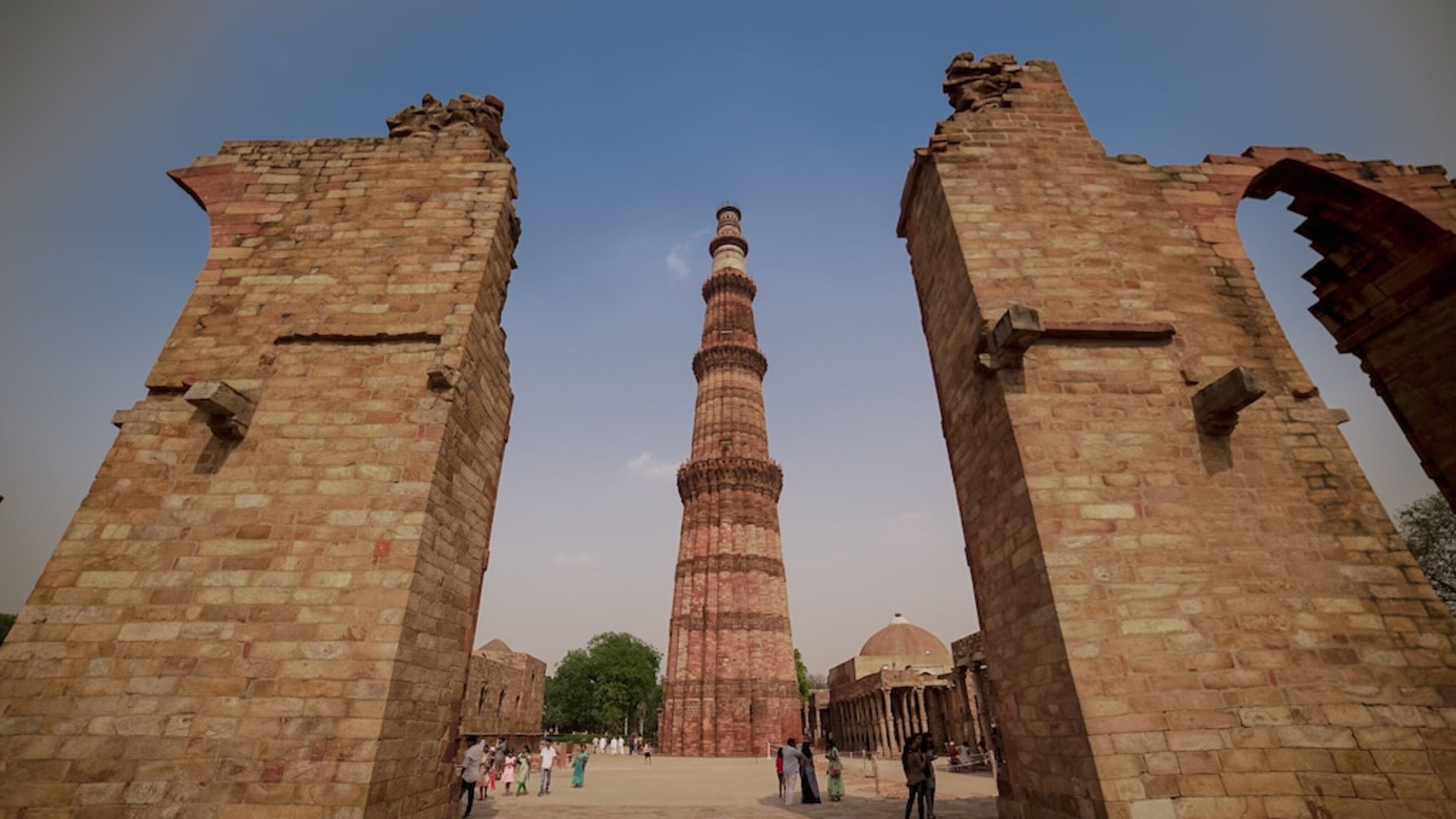 A historic tower with a spiral minaret, flanked by ancient stone arches, likely part of a larger historical complex.