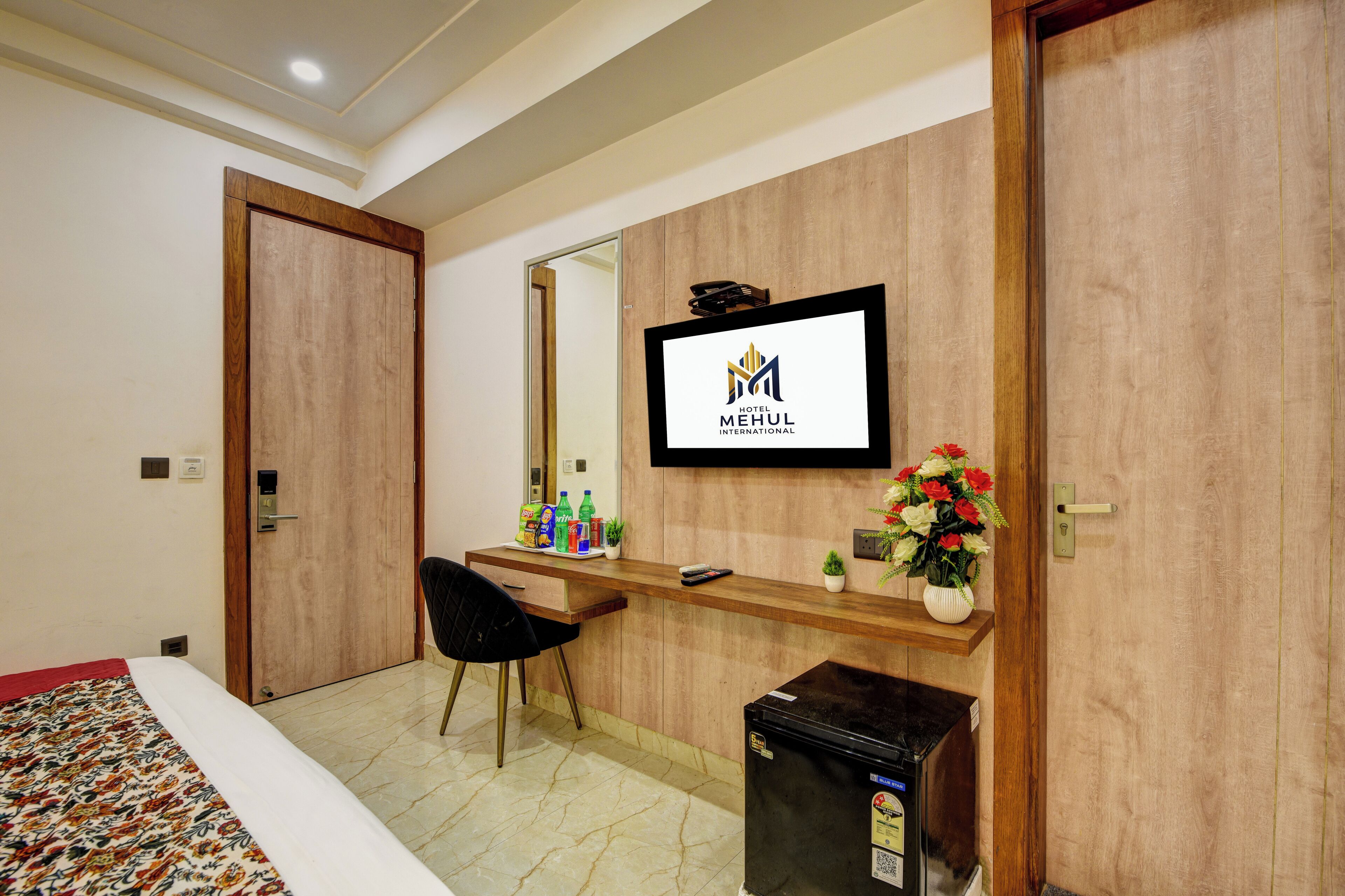 A hotel room with a bed, a desk with a mirror, a television, and a minibar.