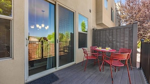 A patio with a table and chairs, a sliding glass door, and a wooden fence.