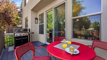 An outdoor patio with a red table, chairs, a grill, and a glass of orange juice.