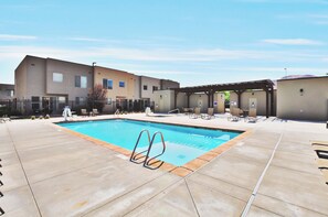 A swimming pool with a sunshade area, a covered seating area, and a building with multiple windows. - Entrada at Moab 624 (Moab)