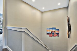 A hallway with a staircase, a wall-mounted artwork depicting a sunset over a rock formation, and a small decorative item on the wall. - Entrada at Moab 624 (Moab)