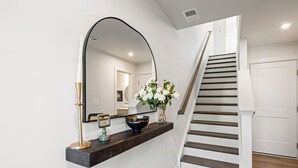 A modern interior with a dark wood console table, a large mirror, a vase with white flowers, and a staircase with wooden steps.