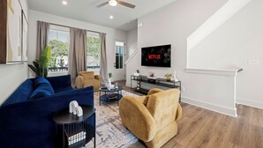 A modern living room with a blue sofa, a yellow armchair, a coffee table, and a TV mounted on the wall.