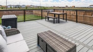 Une terrasse en bois avec une table et des chaises, un petit espace de rangement et une vue sur une zone verdoyante et des bâtiments au loin.