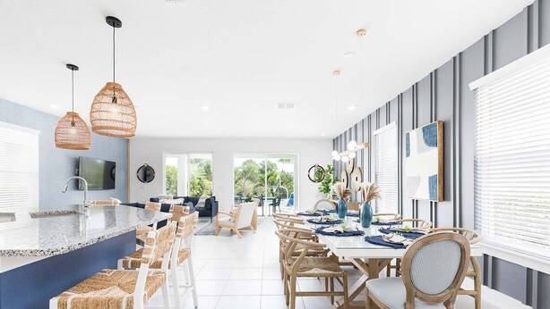 Una cocina moderna con una isla central, armarios blancos y un comedor con sillas de madera y una mesa blanca.