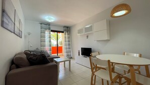 A compact living space with a sofa, a dining table with chairs, a TV, and a balcony with curtains.