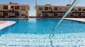 A swimming pool with clear blue water, surrounded by buildings with balconies and covered seating areas.
