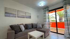 A living room with a sofa, a coffee table, and a balcony with a view of palm trees.