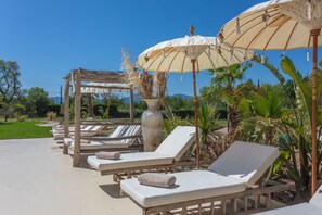 A poolside area with lounge chairs, umbrellas, and a pergola structure.