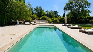 Una piscina rectangular con superficie de agua azul cristalina, rodeada por un solado pavimentado.