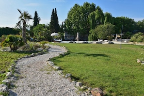 A garden with a gravel path, lounge chairs, and a building with a pergola. - Holiday Home 'Domaine Montserrat' with Mountain View, Private Pool and Wi-Fi (Le Luc)