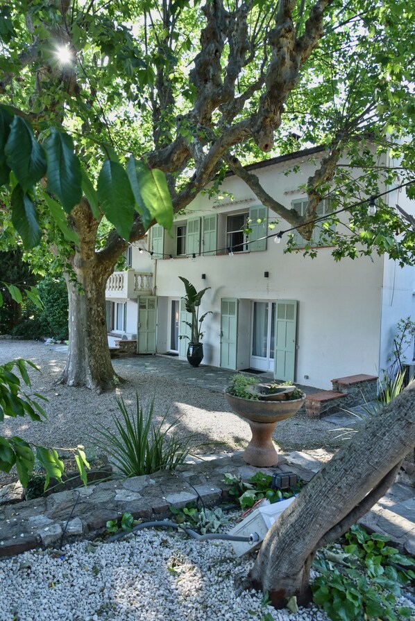 A two-story building with a gravel courtyard, a large tree, and a potted plant. - Holiday Home 'Domaine Montserrat' with Mountain View, Private Pool and Wi-Fi (Le Luc)