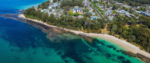 An aerial view of Jervis Bay with a coastal area, clear waters, and a residential zone with houses and greenery.
