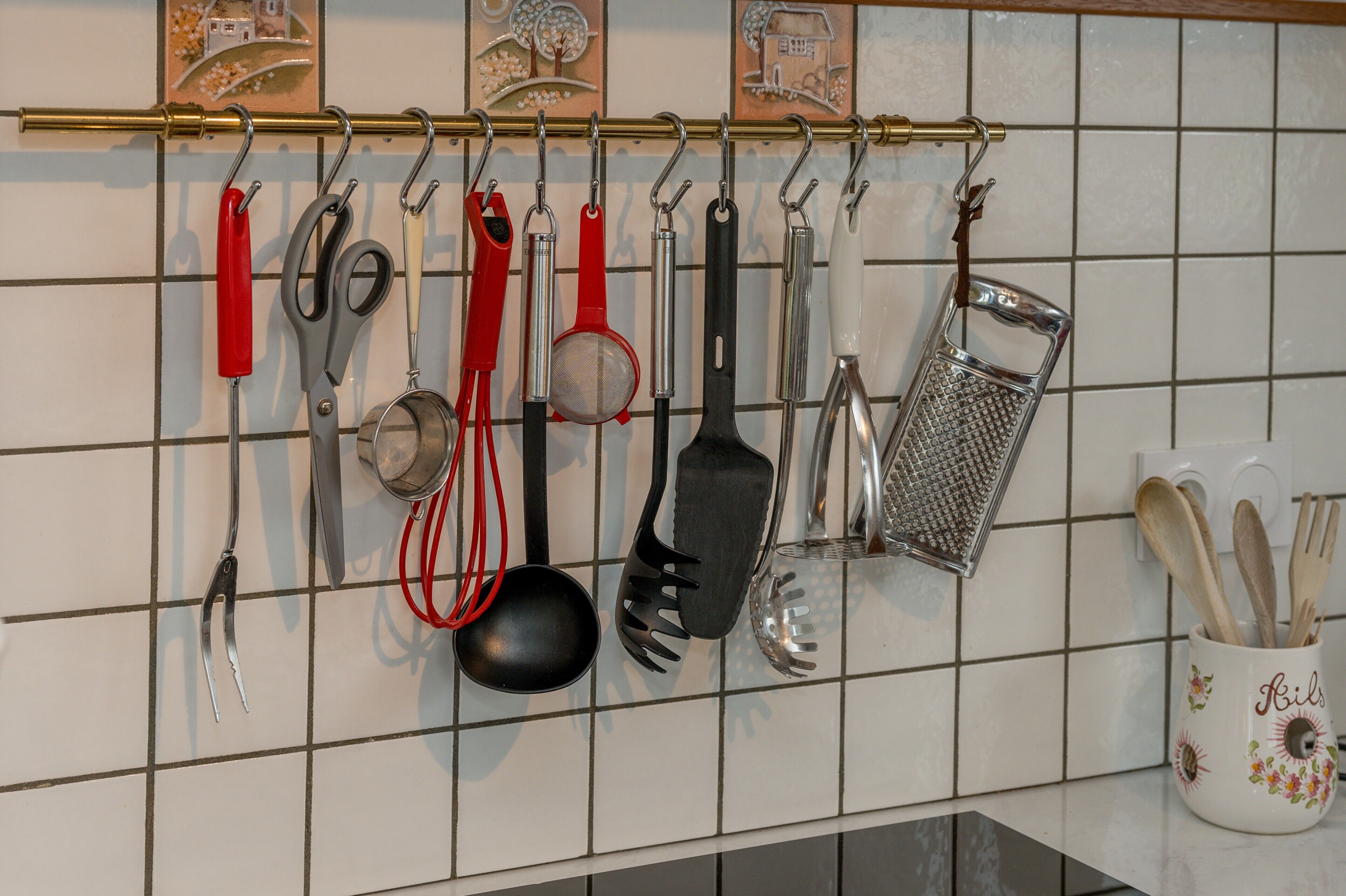 A kitchen with various utensils hanging on a rack, a white tiled backsplash, and a decorative mug with wooden utensils.