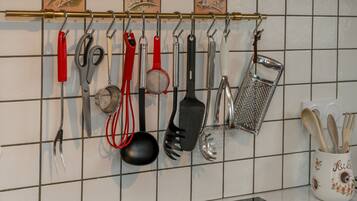 A kitchen with various utensils hanging on a rack, a white tiled backsplash, and a decorative mug with wooden utensils.