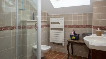 Een badkamer met douche, toilet en wastafel, een handdoekrek en een dakraam.
