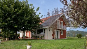 A red house with a sloped roof, surrounded by a well-maintained lawn and potted plants.