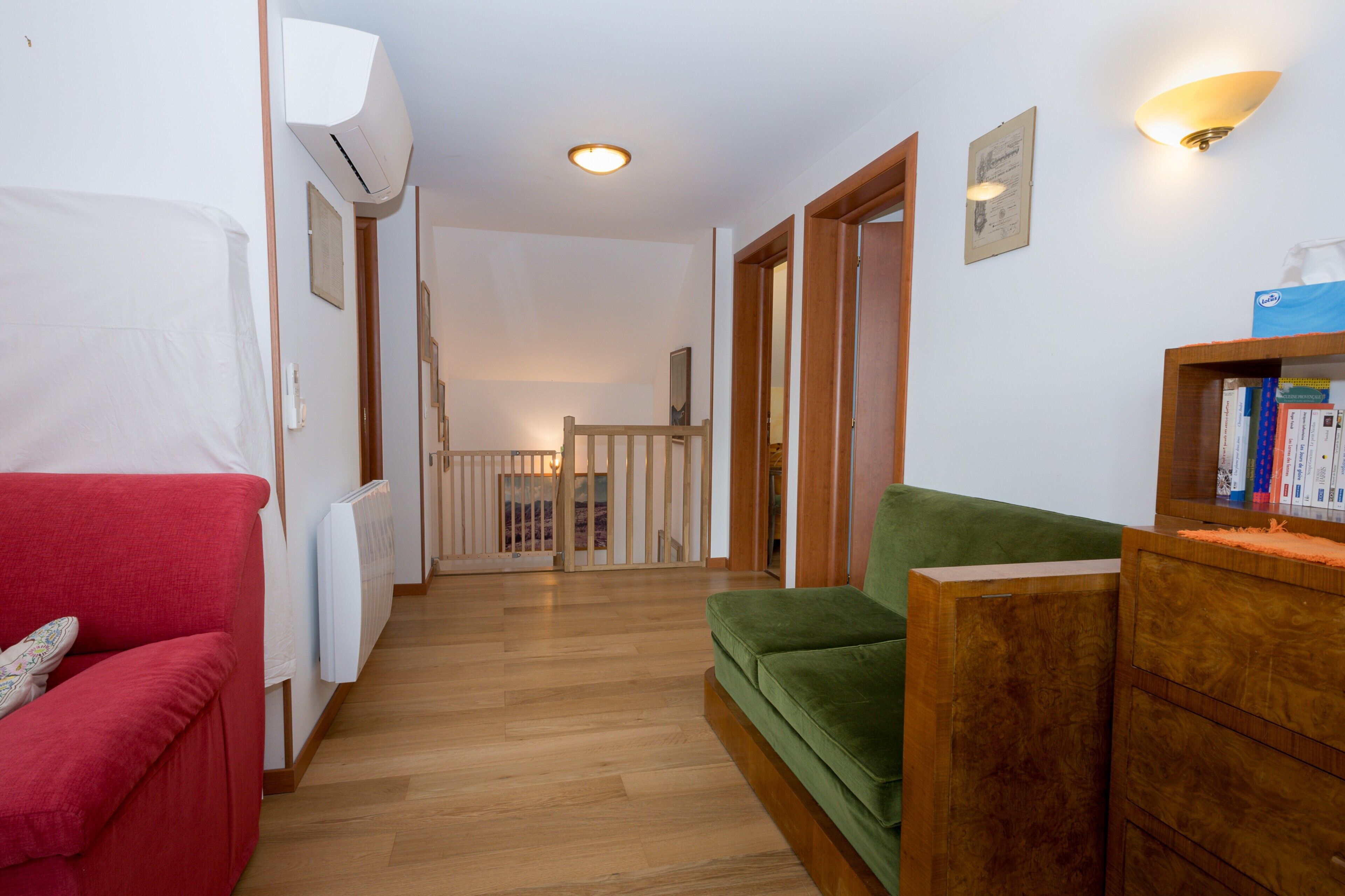 Un couloir avec un canapé rouge, un canapé vert et un meuble en bois rempli de livres.