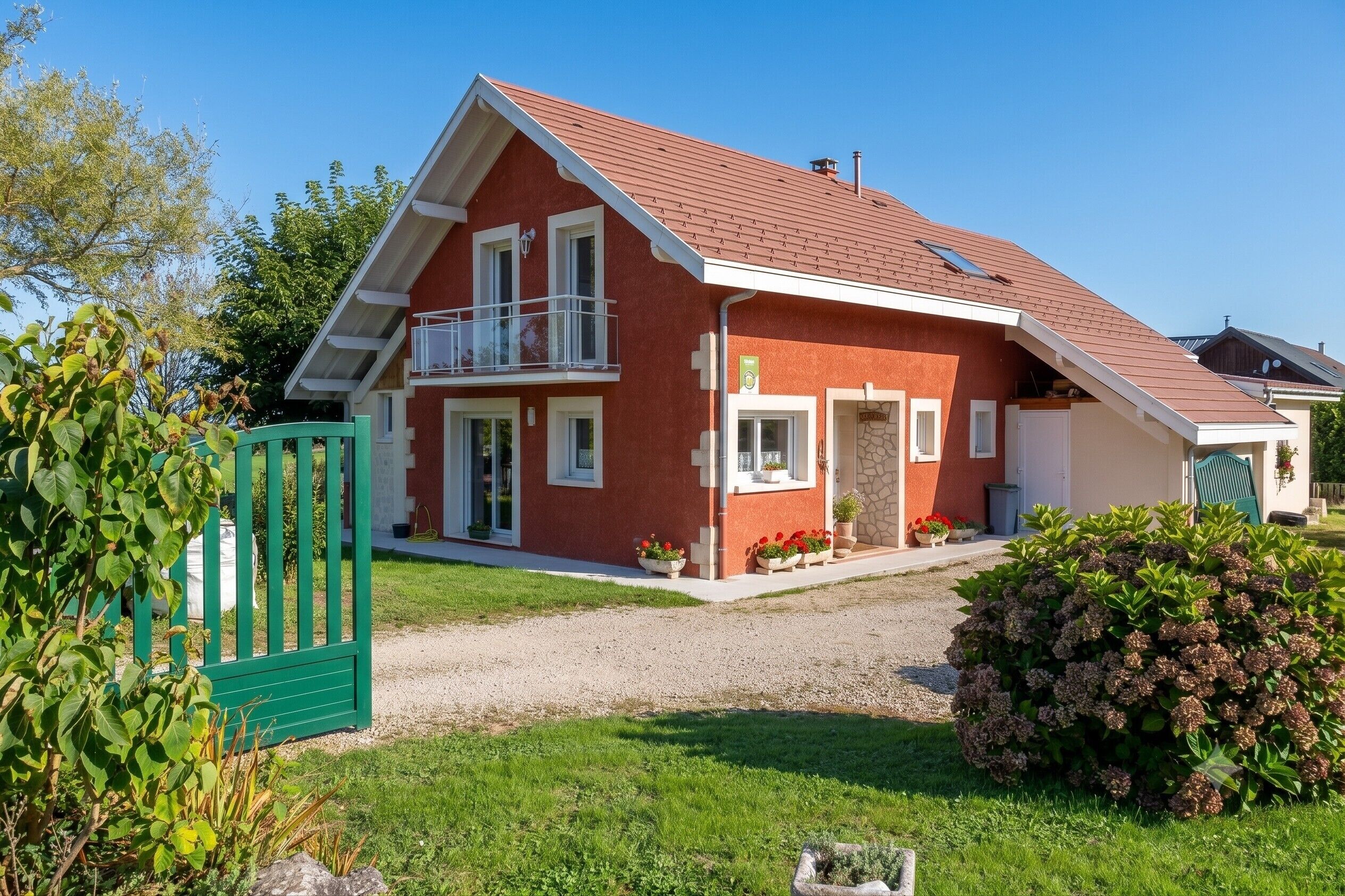Ein zweistöckiges Haus mit roter Fassade, einem Balkon und einer Schotterauffahrt.