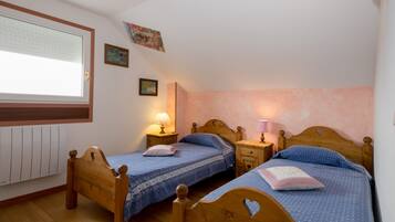 A bedroom with two wooden beds, a window with blinds, a radiator, and wall-mounted lamps.