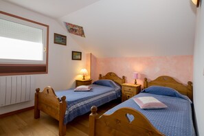 Un dormitorio con dos camas de madera, una ventana con persianas, un radiador y lámparas fijadas a la pared.