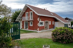A two-story house with a red exterior, a balcony, and a gravel driveway.