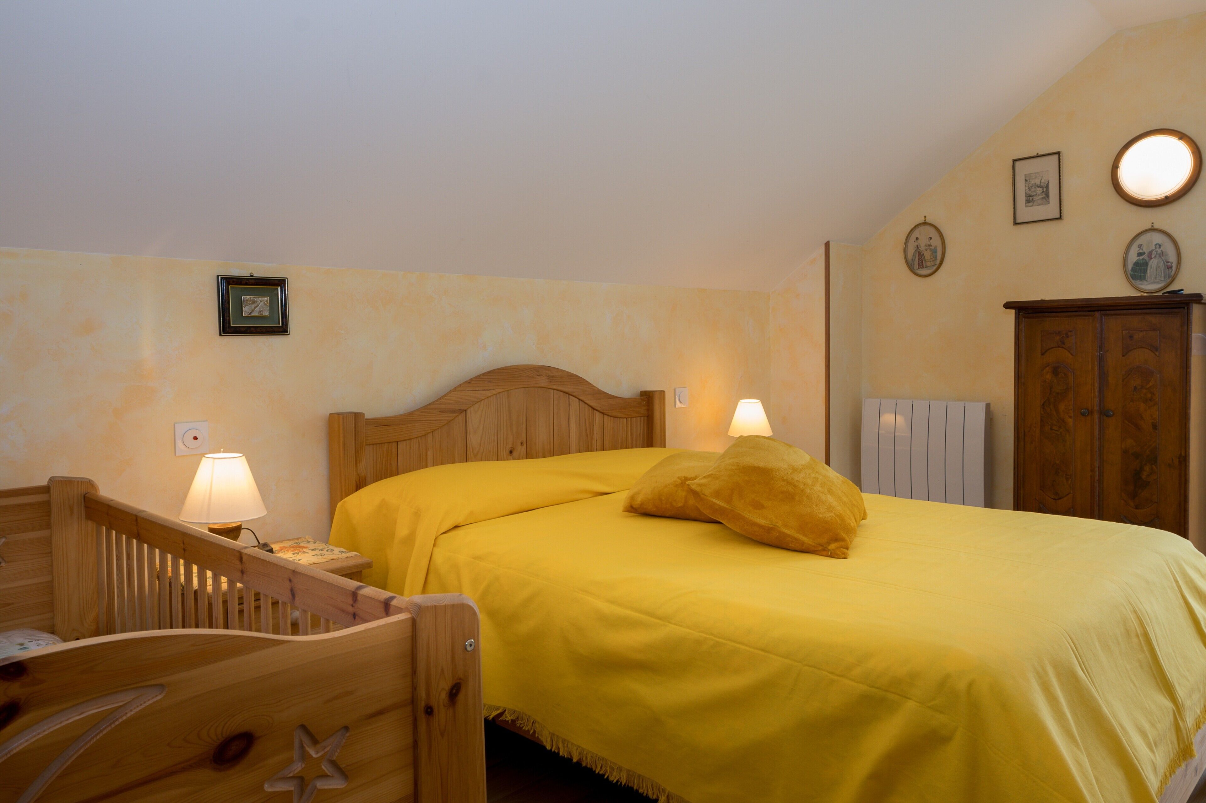 Ein Schlafzimmer mit einem hölzernen Bett, einem Nachttisch, einem Kinderbett und einem Holzschrank.