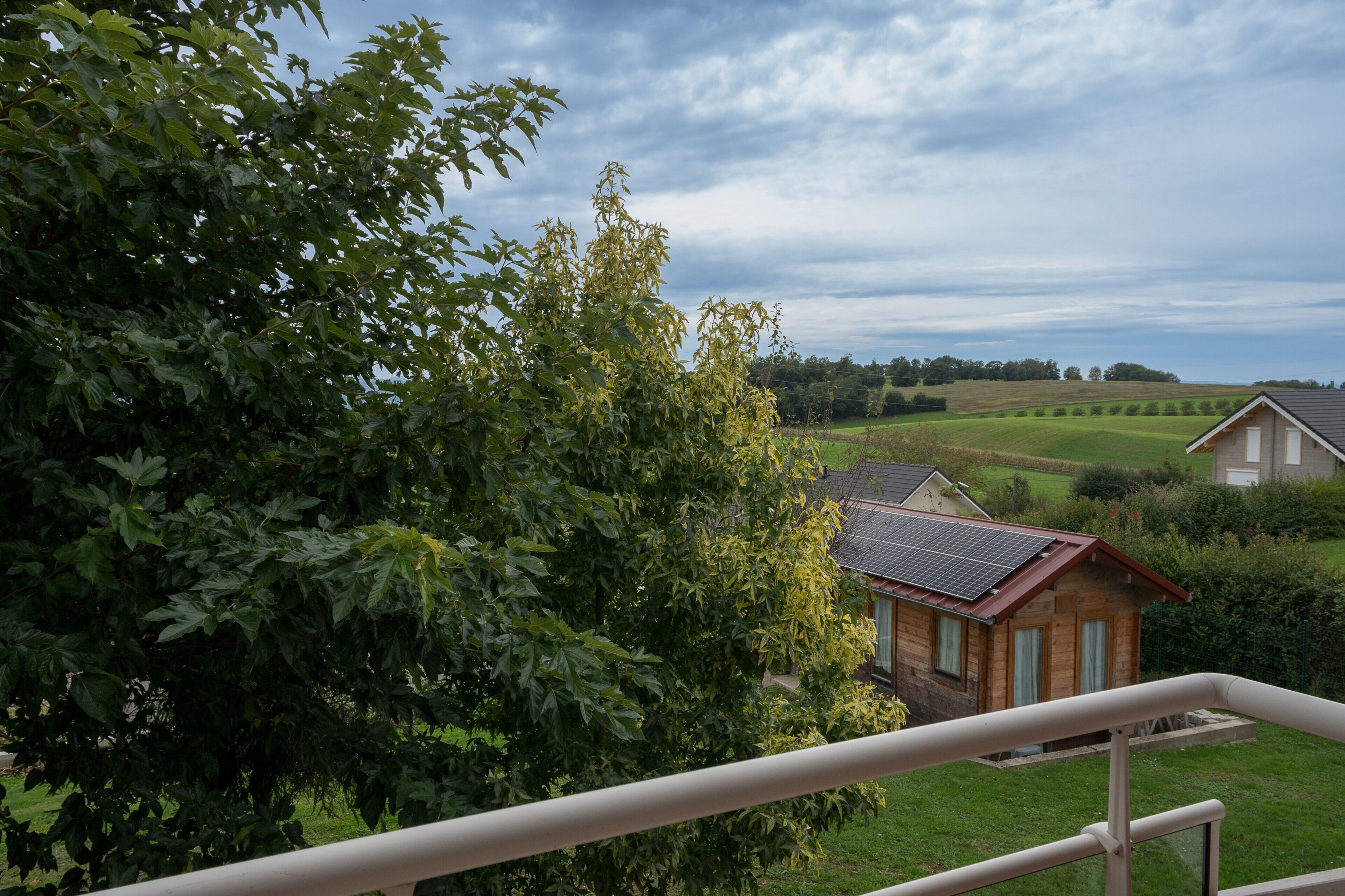 Una casa con techo inclinado, rodeada de abundante vegetación y cielo despejado.
