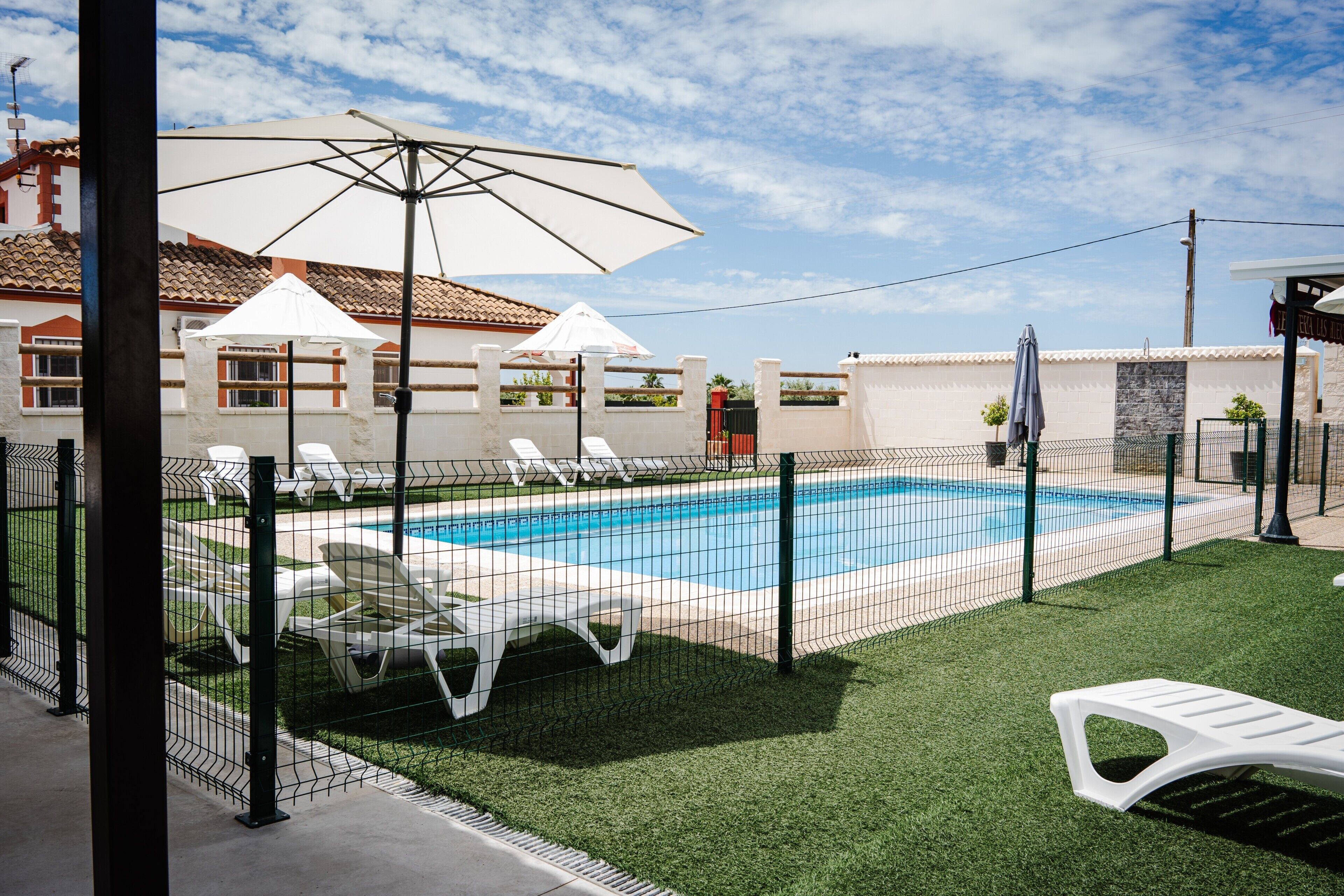 A swimming pool with a fence, white lounge chairs, and umbrellas.