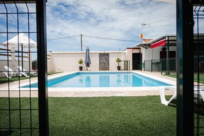 A swimming pool with a tiled deck, surrounded by artificial grass, and a fenced area with lounge chairs.