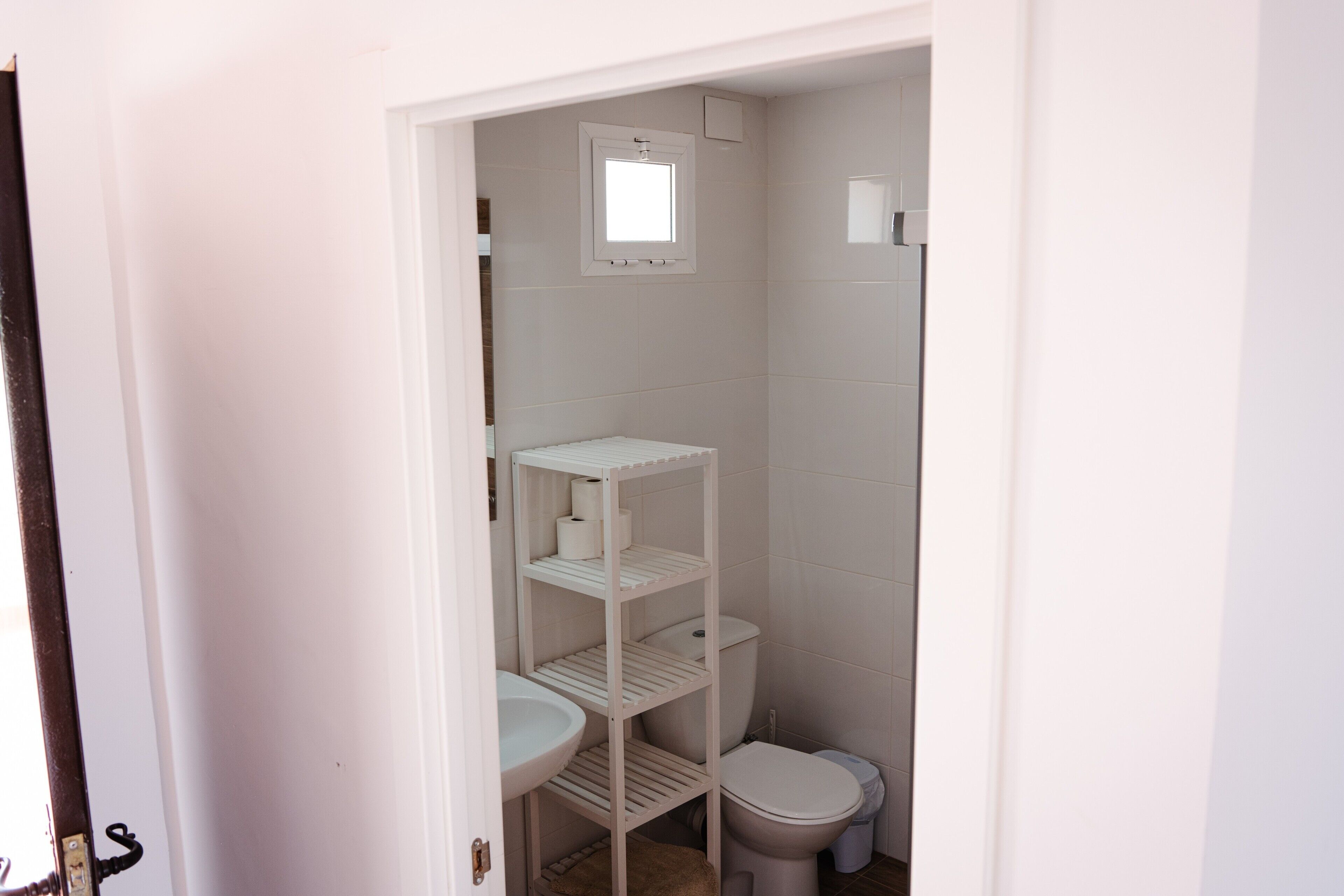 Ein kleines, weißes Badezimmer mit Toilette, Waschbecken und Ablagefläche.