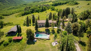 Propiedad rural con piscina, una casa grande y follaje circundante.