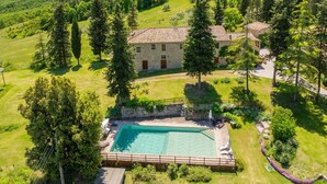Una casa de piedra con piscina, rodeada de árboles y un paisaje montañoso.