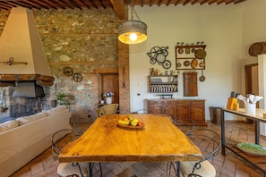A rustic kitchen with a wooden table, stone wall, and various kitchen utensils.